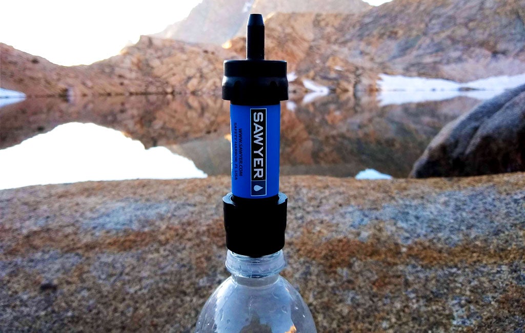 Filtro de agua Sawyer y botella de agua inteligente sobre un fondo de lago