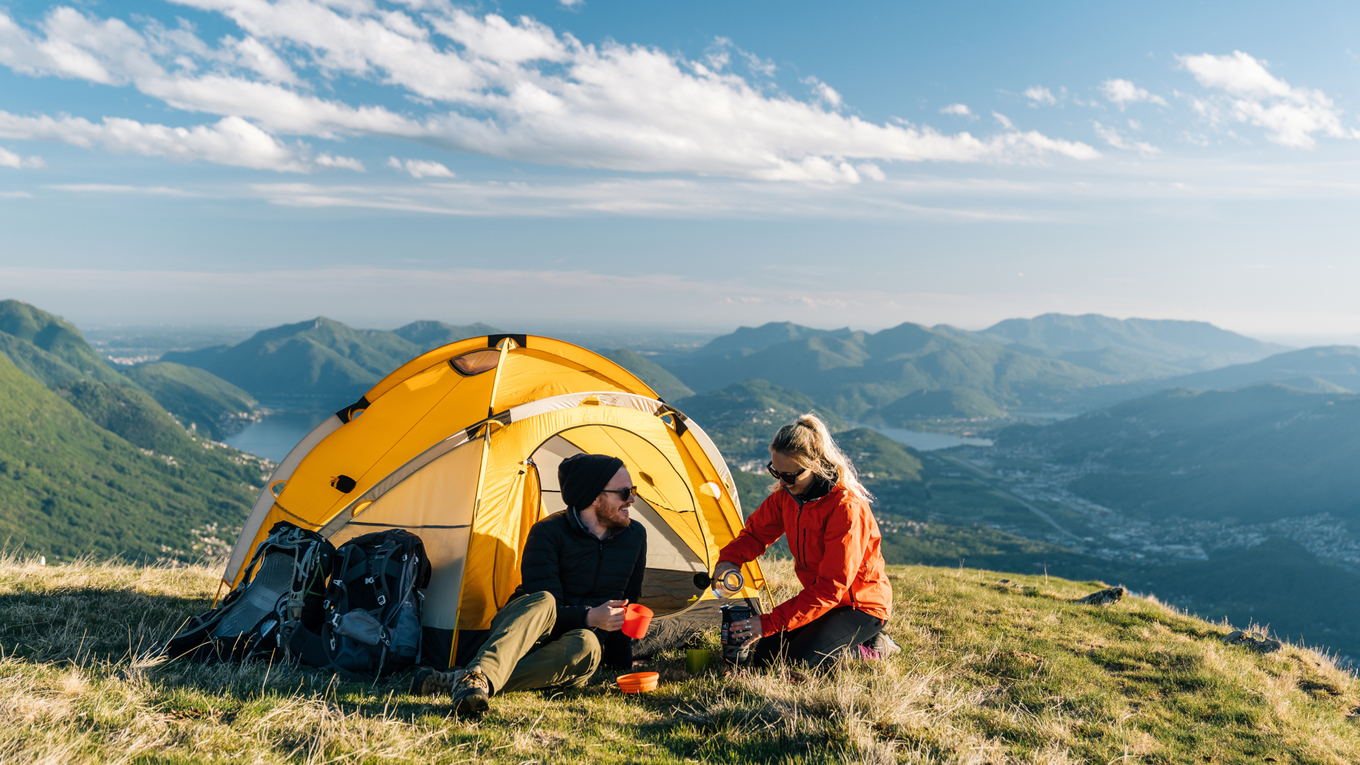Cómo acampar bajo la lluvia: un hombre y una mujer tomando café afuera de su tienda con montañas al fondo