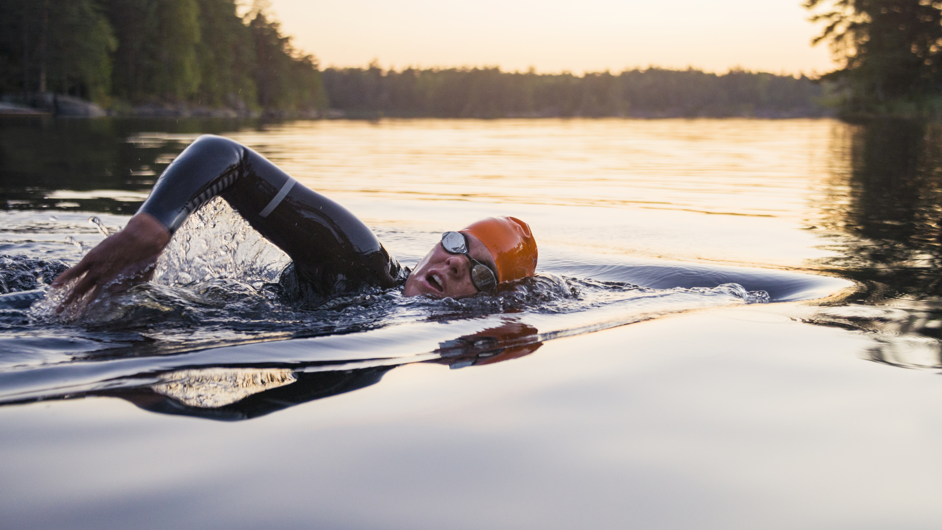 Una persona nadando en un lago al atardecer.