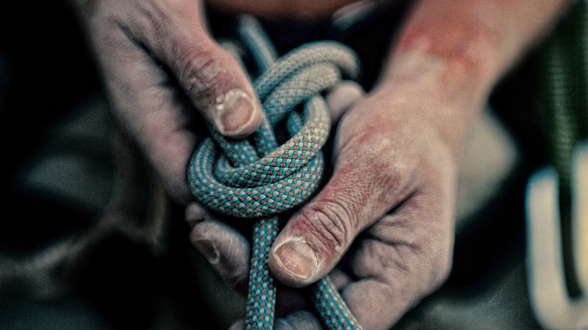 Primer plano de manos calcáreas atando una cuerda de escalada en un nudo
