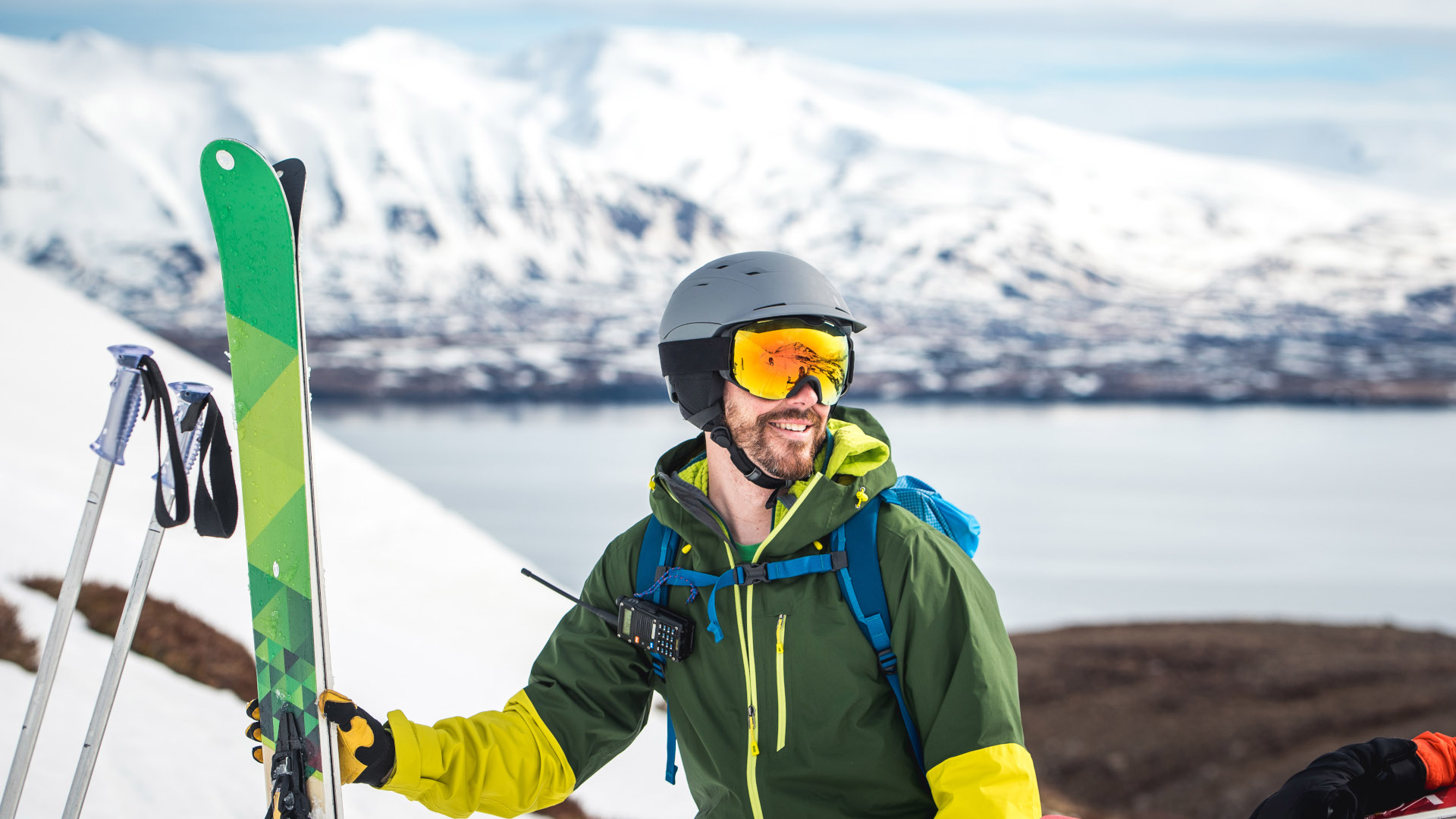 Un esquiador sujeta sus esquís y charla con un amigo con un lago de fondo