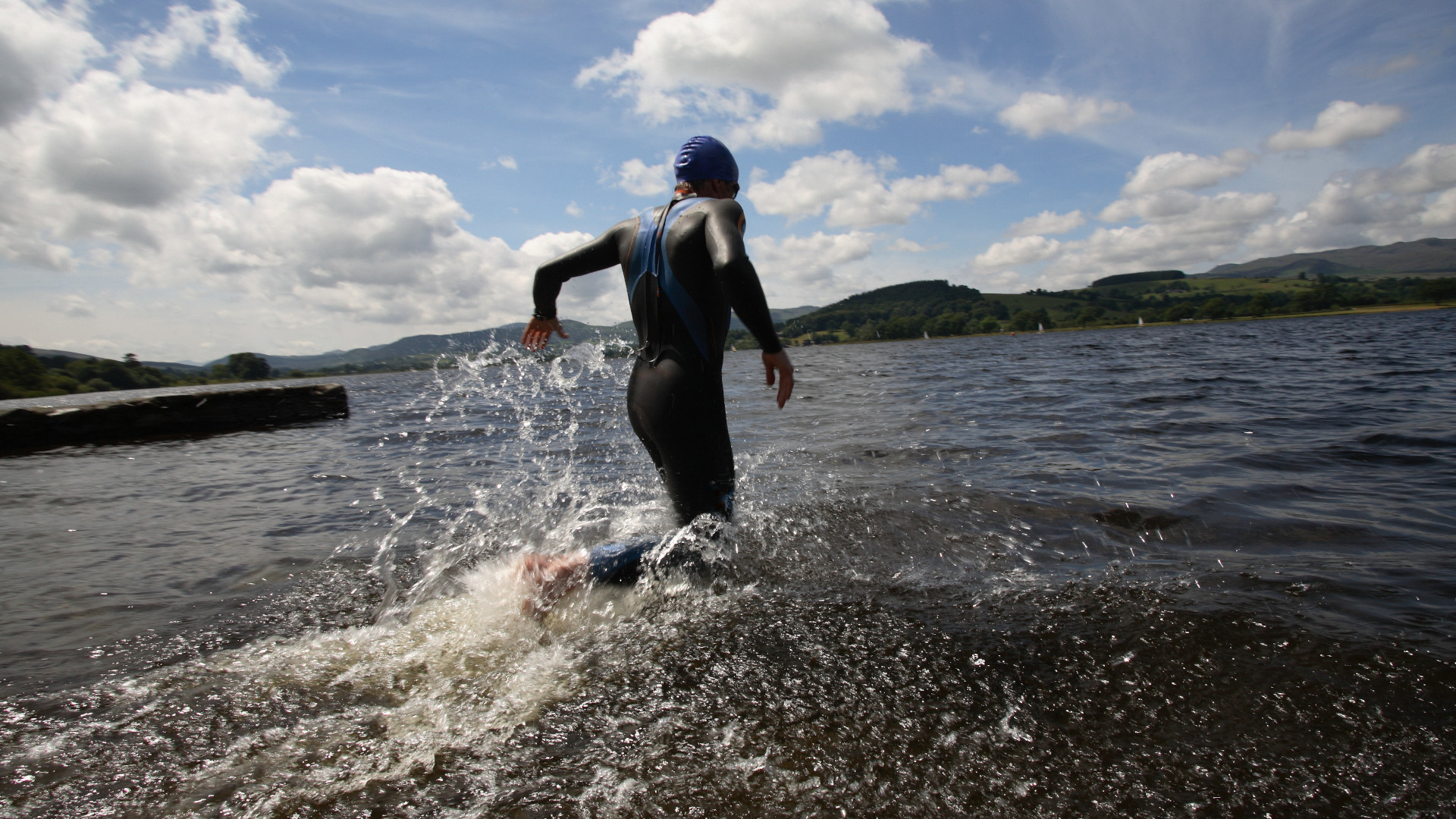 Un nadador en traje de neopreno corre hacia el agua.