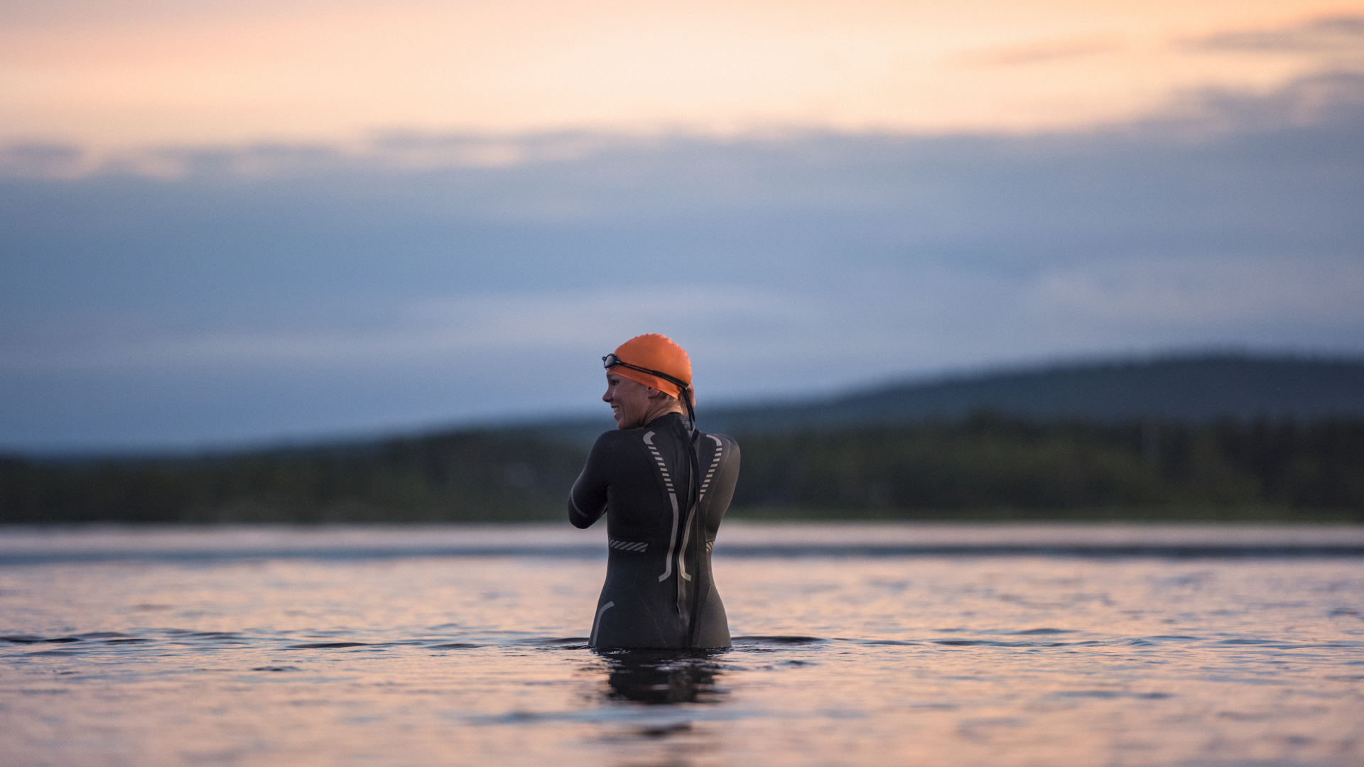 Una mujer en traje de neopreno entrando en un lago para nadar salvajemente al atardecer