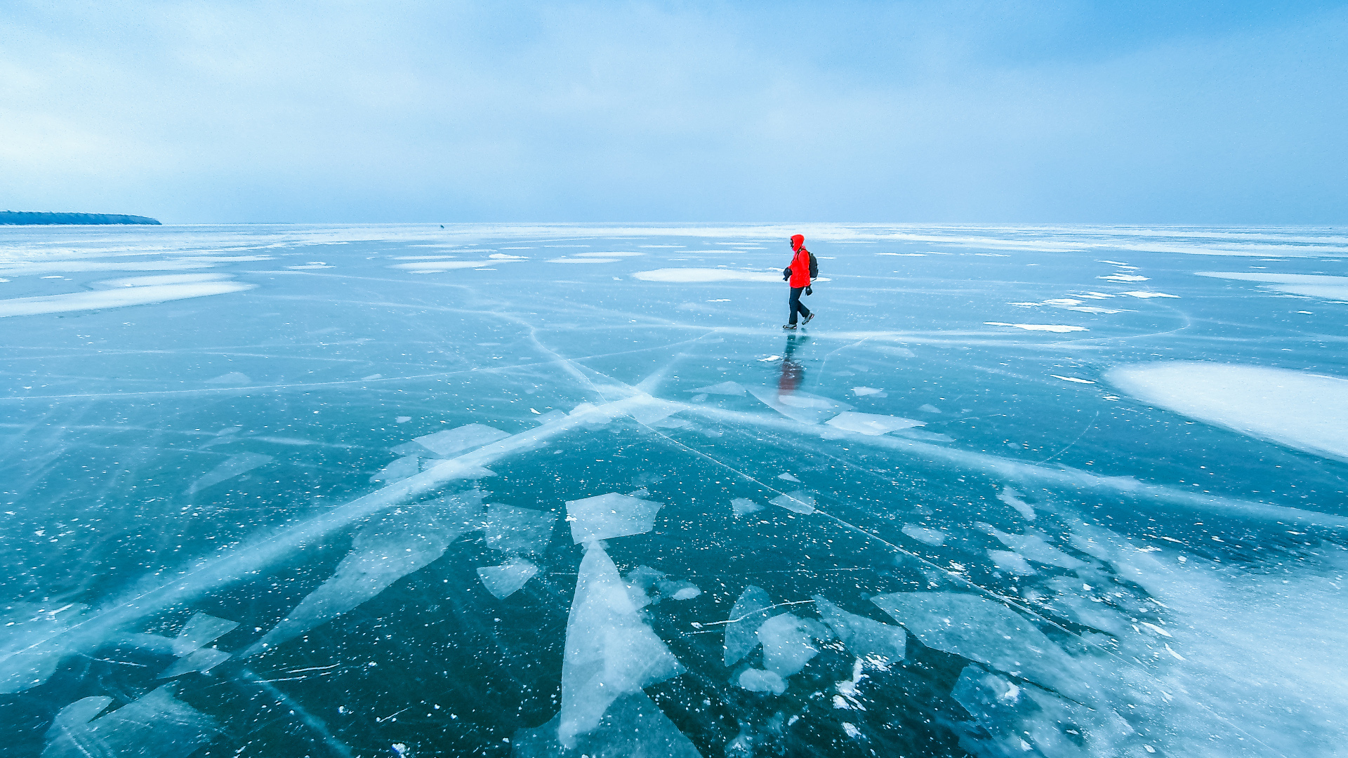 Una mujer con un abrigo rojo cruzando un lago congelado