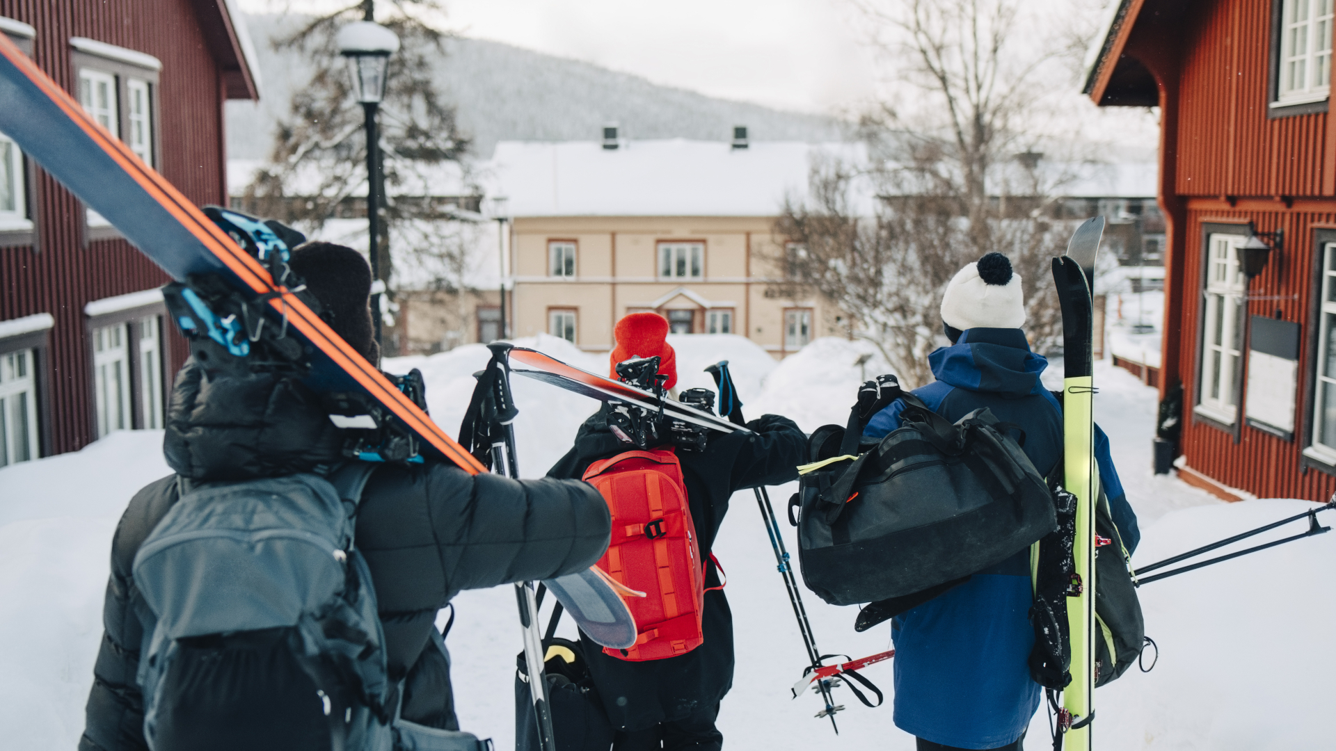 Tres esquiadores paseando por un resort con los esquís al hombro