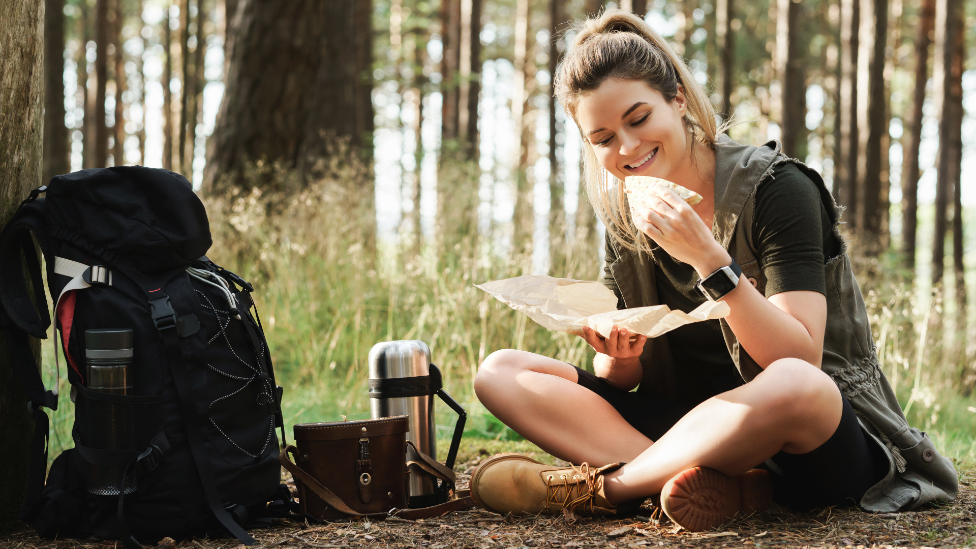 Un excursionista comiendo un sándwich en el bosque.