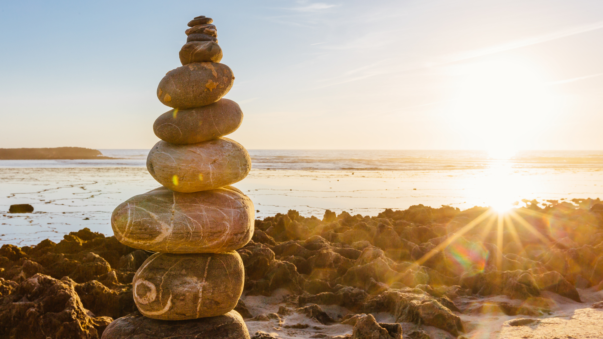 Piedras apiladas en una playa con puesta de sol al fondo