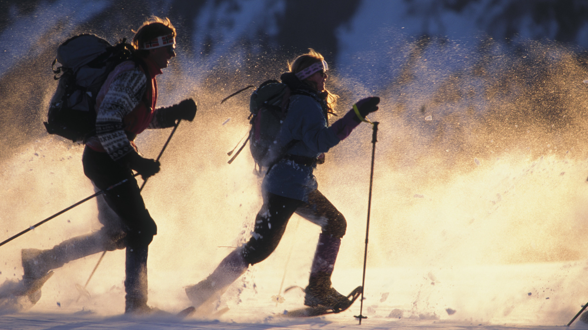 Dos personas corriendo con raquetas de nieve al atardecer