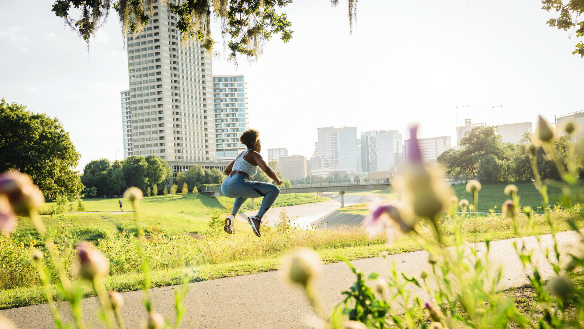 Mujer en cuclillas saltando sobre la ruta de carrera en el parque más allá de las flores silvestres