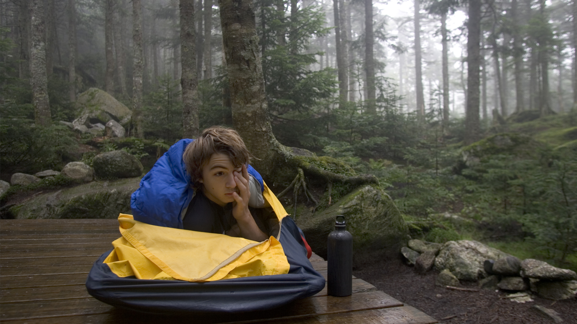 Un adolescente se despierta en una bolsa bivvy en un campamento en la naturaleza