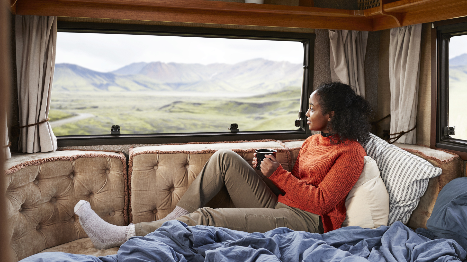 Una mujer se sienta en su caravana con té admirando la vista a la montaña