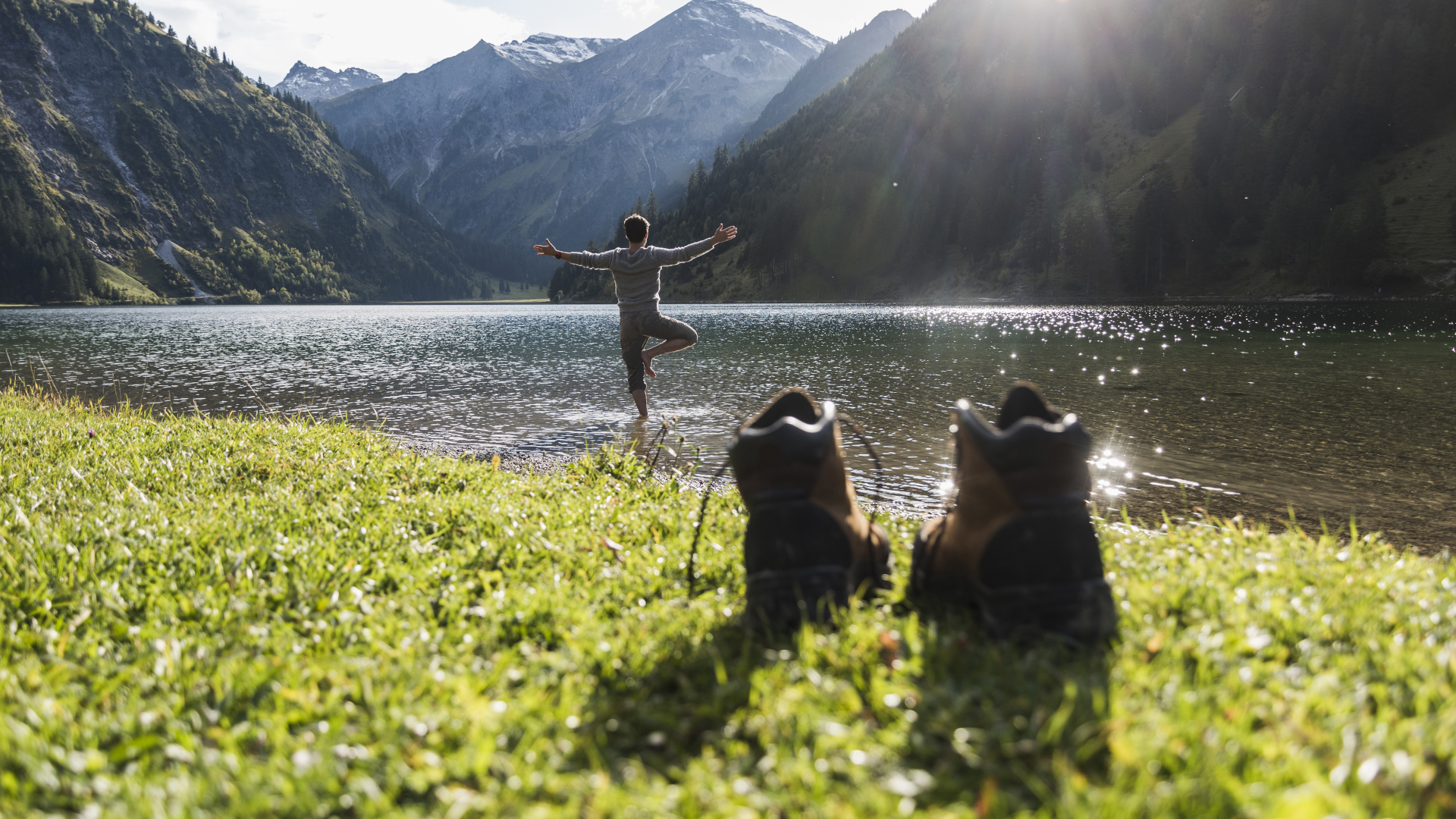 Un hombre haciendo yoga junto a un lago con botas de montaña en primer plano