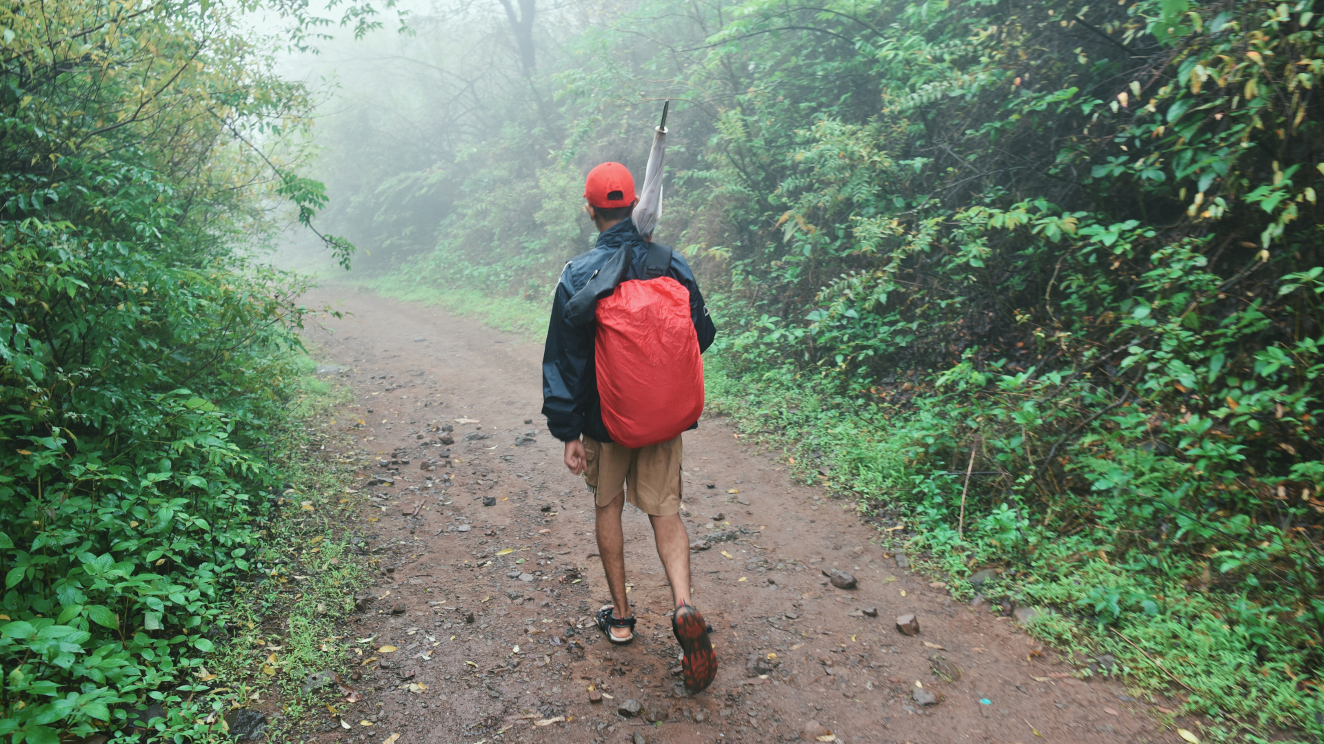 Un hombre camina por un sendero con una cubierta impermeable en su mochila.