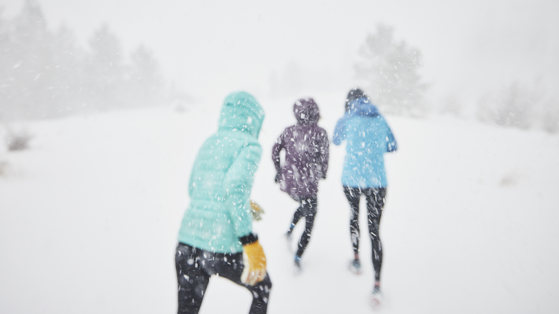 Tres mujeres corriendo cuesta arriba en la nieve.